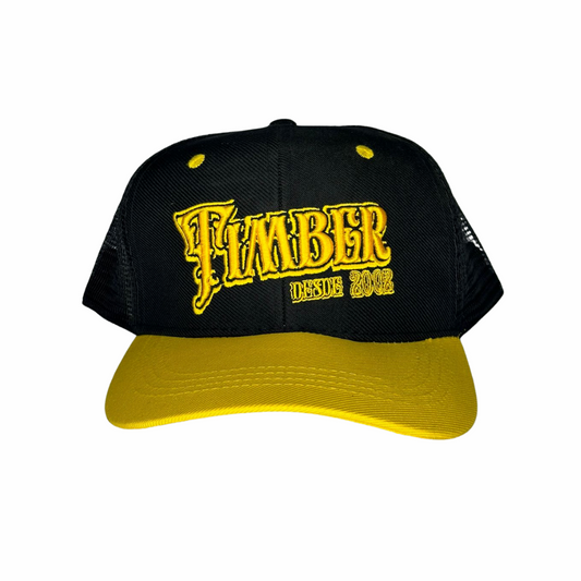 O boné apresenta um painel frontal preto com o bordado "Timber desde 2002" em um estilo clássico, destacado pelo contraste com o amarelo brilhante. A aba amarela cria um design dinâmico e marcante.