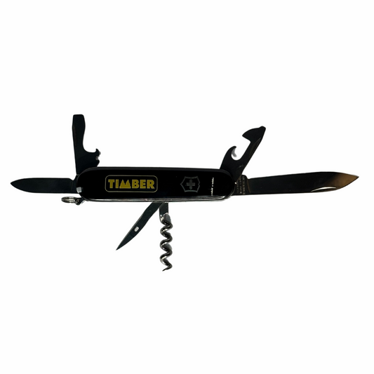 Um canivete multifuncional na cor preta com detalhes metálicos. Está aberto, exibindo várias ferramentas, incluindo lâminas, abridor de garrafas, saca-rolhas e outros acessórios. Na lateral, o logo "TIMBER" em amarelo se destaca junto ao símbolo da Suiça.