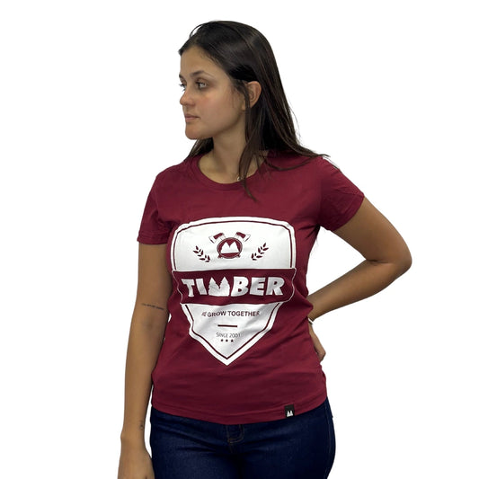 Modelo usando camiseta vermelha feminina 100% algodão com estampa branca 'TIMBER' e slogan 'We Grow Together'.
