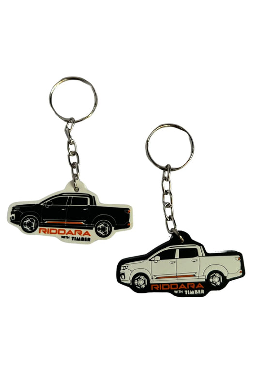 Chaveiro emborrachado no formato de uma caminhonete, com fundo branco e contornos em preto. Detalhes em laranja destacam o nome "RIDDARA with TIMBER". Corrente metálica com argola para chave.