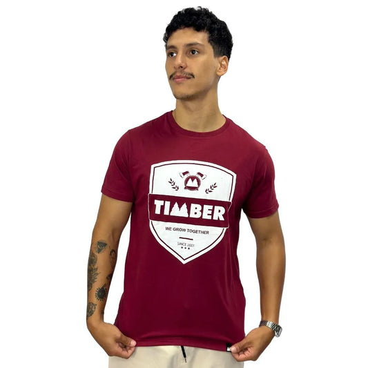 Modelo usando camiseta vermelha masculina 100% algodão com estampa branca 'TIMBER' e slogan 'We Grow Together'.