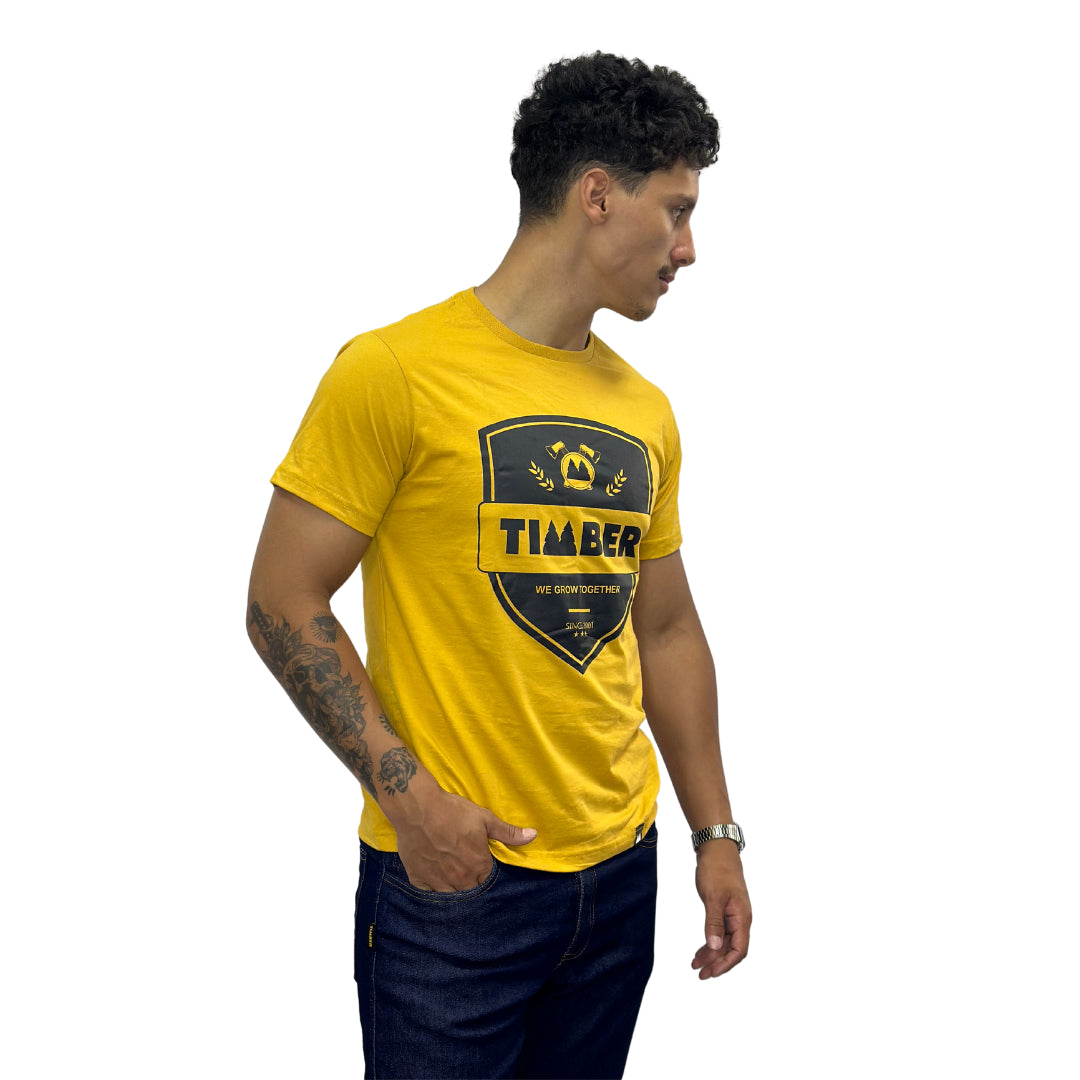 Modelo usando camiseta amarela masculina 100% algodão com estampa preta 'TIMBER' e slogan 'We Grow Together'.